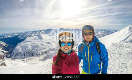 Un paio di sci outfits permanente sulla cima di una montagna innevata e godersi la giornata di sole. Entrambi sono ridendo e godendo della vista. Tall Foto Stock