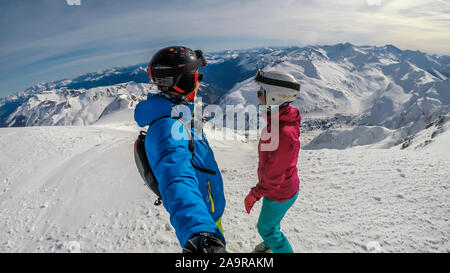 Un paio di sci outfits permanente sulla cima di una montagna innevata e godersi la giornata di sole. Entrambi sono ridendo e godendo della vista. Tall Foto Stock