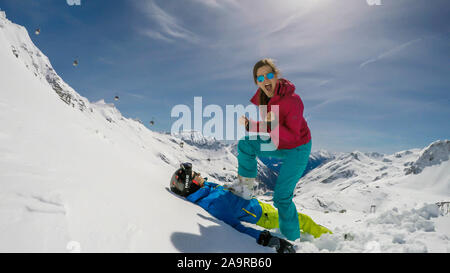 Un paio di sci outfits giocando nella polvere di neve. La ragazza è in piedi con un piede sul ragazzo, come se lei lo ha battuto. Lei è felice e trionfante. Fine Foto Stock