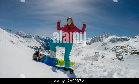 Un paio di sci outfits giocando nella polvere di neve. La ragazza è in piedi con un piede sul ragazzo, come se lei lo ha battuto. Lei è felice e trionfante. Fine Foto Stock