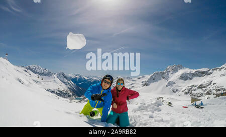 Un paio di sci outfits giocando nella polvere di neve. Essi stanno lanciando palle di neve e ridere a voce alta, tempo di gioco. Gamme infinite di neve tappata mou Foto Stock