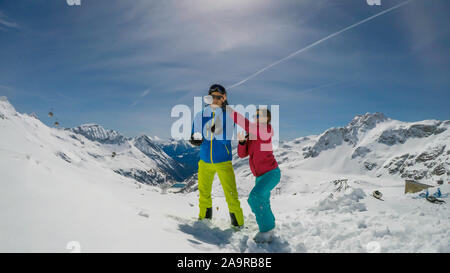 Un paio di sci outfits giocando nella polvere di neve. Essi stanno lanciando palle di neve e ridere a voce alta, tempo di gioco. Gamme infinite di neve tappata mou Foto Stock
