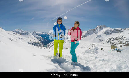 Un paio di sci outfits giocando nella polvere di neve. Essi stanno lanciando palle di neve e ridere a voce alta, tempo di gioco. Gamme infinite di neve tappata mou Foto Stock