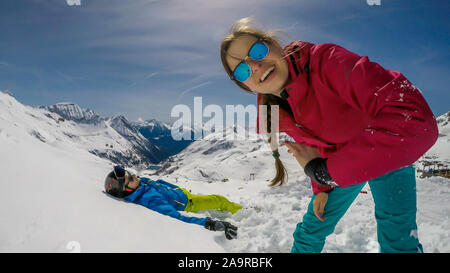 Un paio di sci outfits giocando nella polvere di neve. Il ragazzo è disteso sulla neve e una ragazza sorride alla telecamera. Trascorrere del tempo insieme. Infinite Foto Stock