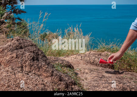 La carità il concetto di ambiente. Mano di uomo il prelievo di lattina della bevanda da terra, cestino di raccolta Foto Stock