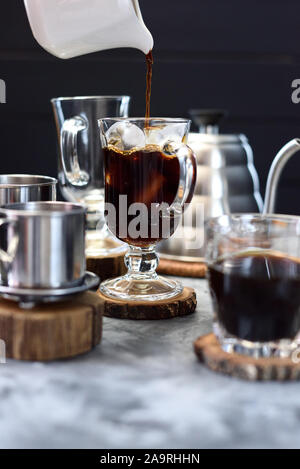 La produzione di ghiaccio in caffè. Versare il caffè nero su ghiaccio nel bicchiere alto su sfondo scuro spazio copia Foto Stock