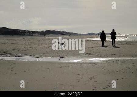 Silhouette di persone e il loro cane a camminare sulla spiaggia in Sintmaartenszee nei Paesi Bassi Foto Stock