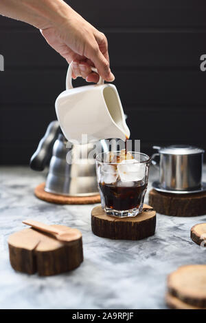 Fare caffè ghiacciato. Donna slanciata mano versando il caffè nero su ghiaccio su sfondo scuro spazio copia Foto Stock