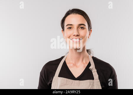 Piuttosto giovane cameriera bruna in grembiule che vi guardano con sorriso toothy Foto Stock