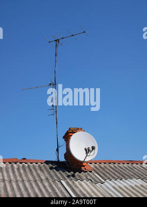 Tv satellitare e varie antenne terrestri installato sul tetto di ardesia di una vecchia casa sullo sfondo di un cielo blu senza nuvole Foto Stock