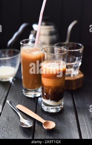 Iced layered il caffè con il latte di cocco e latte condensato in bicchieri alti stile vietnamita su sfondo scuro in verticale Foto Stock