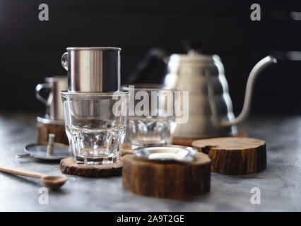 Facendo gocciolare il caffè in stile vietnamita in phin e bicchieri su sfondo scuro fuoco selettivo Foto Stock