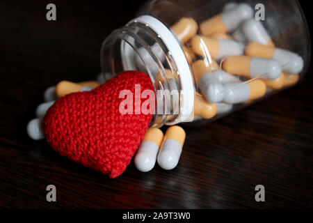 Pillole e lavorati a maglia cuore rosso scuro sul tavolo di legno, bottiglia con farmaci in capsule. Concetto di ipertensione, malattie cardiache, cardiologia, sangue Foto Stock