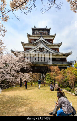 Il castello di Hiroshima in Giappone. La primavera con la fioritura dei ciliegi, il principale ricostruito in stile Borogata mantenere con il quinto piano torre di vedetta con cielo blu. Foto Stock