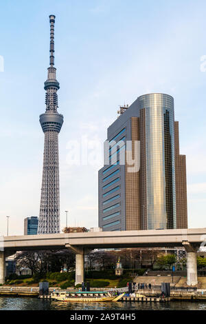 Tokyo Skytree e Sumida Ward ufficio edificio visto dal Tempio di Asakusa. Primo piano, Sumida River con una crociera sul fiume imbarcazione attraccata a tubo piccolo. Ora d'oro Foto Stock