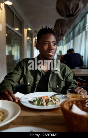 Giovane americano africano l uomo è di mangiare in un ristorante e gustare deliziosi cibi Foto Stock