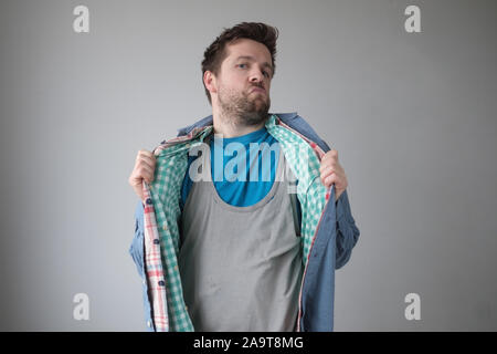 Fumetto effeminato uomo che indossa diversi shirt. Ho messo su tutti i miei abiti migliori. Studio shot Foto Stock