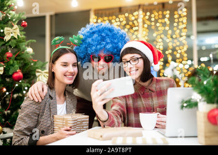 Gruppo di colleghi felice in costumi natalizi rendendo selfie dal luogo di lavoro di Office Foto Stock