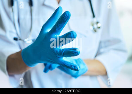 Medico mette su guanti di gomma. isolato su sfondo azzurro. Foto Stock