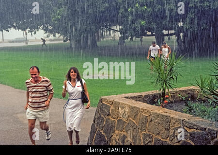 Una doccia a pioggia si riversa giù sul sorpreso i turisti che esegui per trovare rifugio in l'area di Waikiki di Honolulu su Oahu, uno degli otto grandi isole nell'Oceano Pacifico che compongono il tropical stato delle Hawaii, Stati Uniti d'America. Con precipitazioni medie annue di soli 20 a 40 pollici (da 51 a 102 centimetri), Waikiki è più spesso molto asciutto e soleggiato. La cosa migliore di tutti per i visitatori, la pioggia è HIT e MISS -- un minuto può essere di piovere e il minuto successivo il sole splende di nuovo. Foto Stock