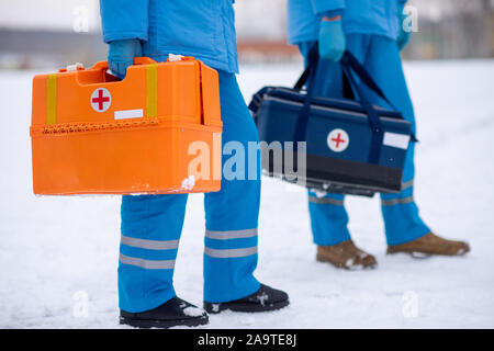 Sezione bassa di due paramedici in uniforme e guanti che trasportano kit di primo soccorso Foto Stock