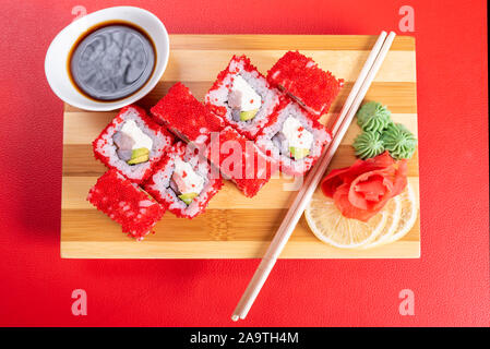 Il Sushi, rotoli in rosso pesci volanti di caviale, con formaggio, avocado e gamberetti. Sulla plancia. Su uno sfondo di colore rosso. Foto Stock