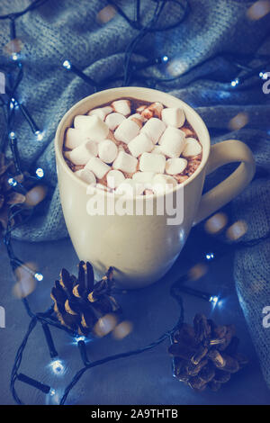 Inverno caldo bevanda a base di cacao e marshmallows in tazza su calcestruzzo con uno sfondo con una ghirlanda di Natale e pigne. Foto Stock