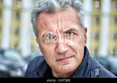 Un curato l uomo con la comparsa di un ufficiale e un arrabbiato reproachful guardare con irritazione guarda nella lente di fotografi contro il retro Foto Stock