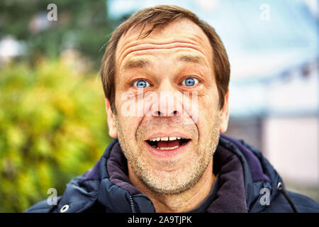 Sorprende il volto di un uomo di cinquanta anni contro lo sfondo di una strada europeo, close-up. Capo di un gioioso di mezza età maschio su 50 outdoo Foto Stock