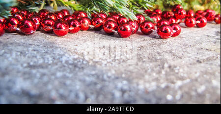 Perle di rosso e rami di conifere su uno sfondo di legno rustico con neve nella giornata di sole. Sfondo per Natale e Anno Nuovo Foto Stock