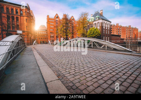 Ponte di arco su canali con acciottolato nella Speicherstadt di Amburgo, Germania, Europa. Storico edificio di mattoni rossi accesi dal tramonto dorato luce n Foto Stock