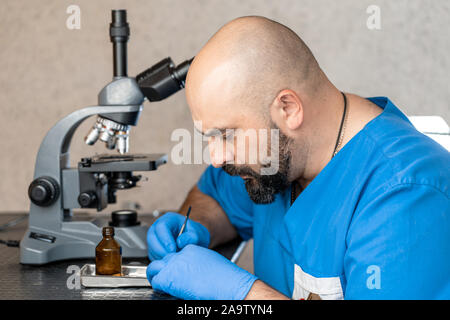 Maschio assistente di laboratorio esaminando campioni di biomateriale in un microscopio. Foto Stock