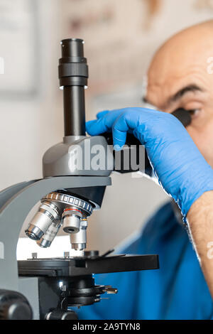 Maschio assistente di laboratorio esaminando campioni di biomateriale in un microscopio. Cllose fino a mani in blu di guanti di gomma regolare il microscopio. Foto Stock