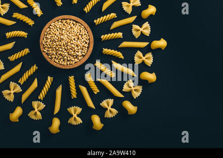 Pasta disposta intorno al mucchio di farina e frumento. Disposti geometrica differente tipo di pasta su sfondo nero. Foto Stock