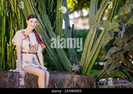 Piuttosto dai capelli rossi ragazza di fronte della fioritura delle piante di cactus in un parco giardino Foto Stock