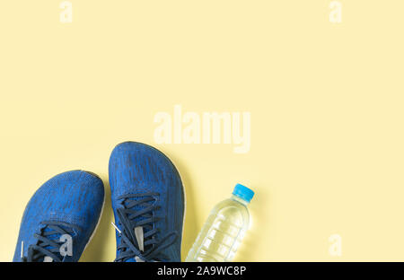 Blue scarpe da corsa e una bottiglia di acqua su sfondo giallo, sport e sano concetto Foto Stock