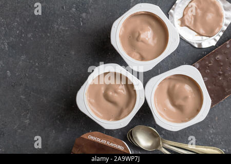 Il cioccolato vasetti per yogurt su Nero - Grigio screziato sfondo con piccoli cucchiai di argento - Tre aromatizzato al cioccolato coppe di yogurt con cioccolato fondente bar su Foto Stock