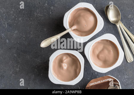 Il cioccolato vasetti per yogurt nero su sfondo a chiazze con piccoli cucchiai di argento - Tre aromatizzato al cioccolato coppe di yogurt Foto Stock