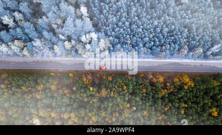 Il confine di autunno e inverno. Corse in auto sulla strada della foresta vista dall'alto del drone. Foto Stock