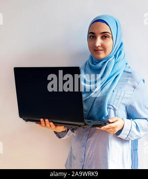 Imprenditrice hijab come avente una chat video sul computer portatile. Carino donna musulmana in tradizionali abiti islamici - hijab tenendo in mano notebook nero Foto Stock