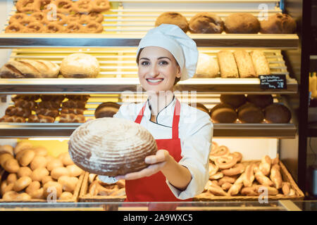 Commessa con grembiule presentando il pane fresco in un panificio Foto Stock