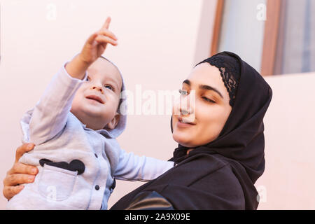 Piccolo bimbo kid nelle mani della madre, felice famiglia musulmana. Baby boy puntando con il dito verso l'alto per mostrare qualcosa a sua madre. Un musulmano Foto Stock
