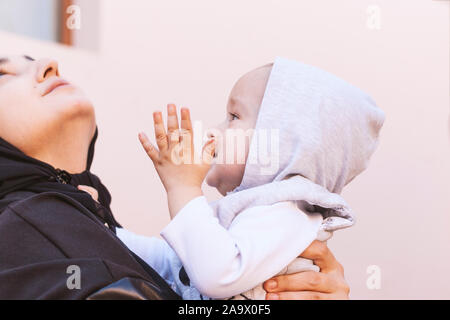 Piccolo bimbo kid nelle mani della madre, felice famiglia musulmana. Baby boy puntando con il dito verso l'alto per mostrare qualcosa a sua madre. Un musulmano Foto Stock