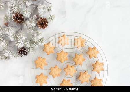 Stella di Natale i cookie in raffreddamento per rack con ramo di sempreverdi e pigne su marmo bianco sfondo con copia spazio. Vista dall'alto. Foto Stock