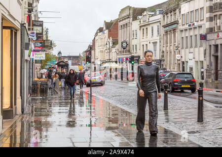 La vistosa Walking donna statua in bronzo dello scultore Sean Henry estensione attraverso Colchester High Street. Foto Stock