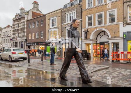 La vistosa Walking donna statua in bronzo dello scultore Sean Henry estensione attraverso Colchester High Street. Foto Stock