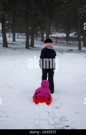 Felice madre con bambino slittino nel parco innevato per le vacanze invernali Foto Stock