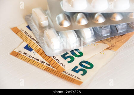 Pillole di medici e di confezioni di farmaco in denaro euro banconote background come un simbolo di spese sanitarie su un tavolo bianco Foto Stock