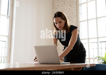 Preoccupato per il giovane imprenditrice appoggiata sopra il tavolo, digitando la risposta al messaggio di posta elettronica. Foto Stock
