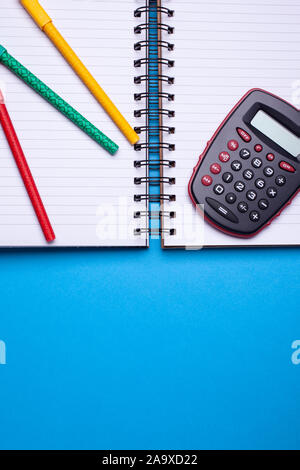 Laici flat top view mockup foto di spazio lavoro con calcolatrice tascabile, penne e copybook blu su sfondo color pastello. Foto Stock